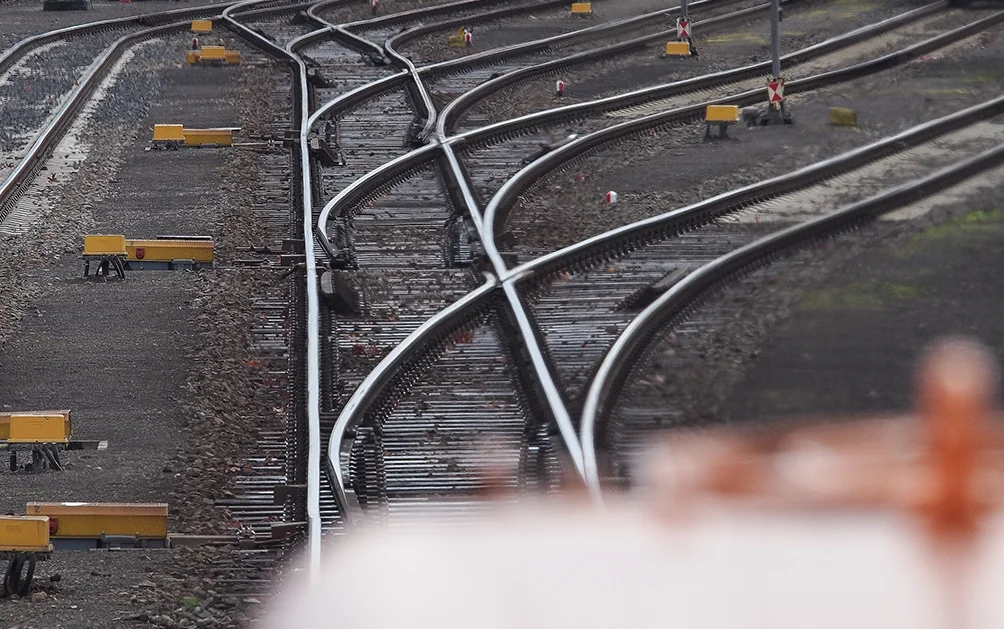 Mehrere verzweigte Eisenbahngleise mit Weichen in einem Gleisfeld, umgeben von Schotterbett und gelben Gleissperren. Blickrichtung entlang der Gleise in leichtem Teleobjektiv-Effekt